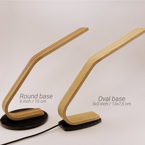 May include: Two wooden table lamps with a curved design. The lamp on the left has a round base, 6 inches in diameter. The lamp on the right has an oval base, 5x3 inches. Both lamps have a black base.