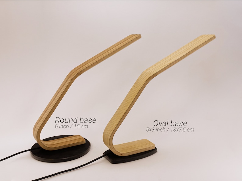 May include: Two wooden table lamps with a curved design. The lamp on the left has a round base, 6 inches in diameter. The lamp on the right has an oval base, 5x3 inches. Both lamps have a black base.