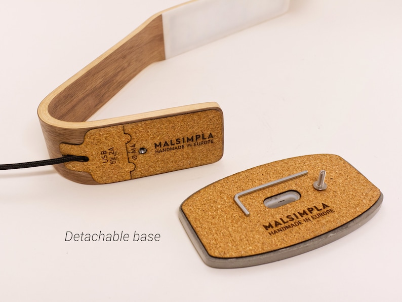 May include: A wooden desk lamp with a cork base. The lamp has a USB port and a detachable base. The base has a screw and a small Allen wrench. The lamp is labeled "MALSIMPLA HANDMADE IN EUROPE".