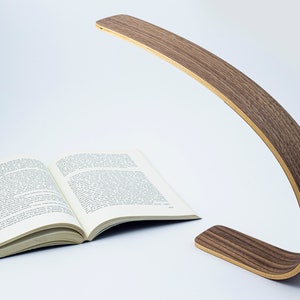May include: A wooden desk lamp with a curved arm and a natural wood finish. The lamp is turned on and illuminating a book.