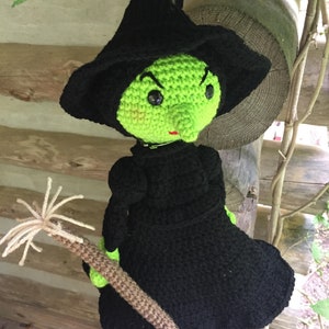 May include: A green and black crocheted witch doll with a pointed hat and a broom. The doll has a green face with black eyes and a red mouth.