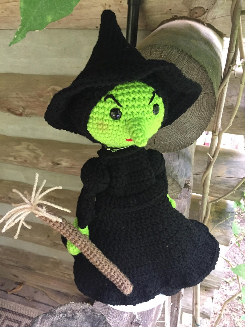 May include: A green and black crocheted witch doll with a pointed hat and a broom. The doll has a green face with black eyes and a red mouth.
