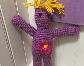 May include: A purple crocheted doll with yellow yarn hair, embroidered eyes, and a pink flower on its stomach.