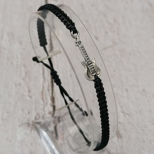 May include: Black braided bracelet with a silver guitar charm.