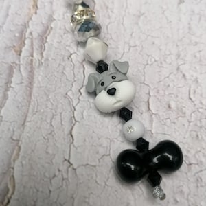 Puede incluir: Un abalorio de cuentas blanco y negro con un pequeño abalorio de perro gris y blanco y un abalorio de lazo negro.