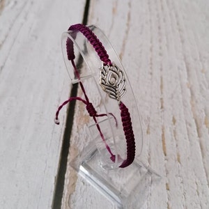 May include: A burgundy braided bracelet with a silver charm in the shape of a stylised feather.