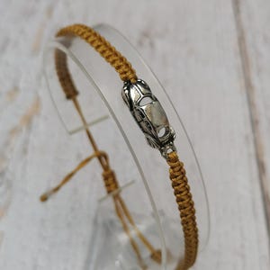Puede incluir: Pulsera de macram&eacute; color mostaza con un dije de coche plateado. La pulsera es ajustable con nudos corredizos. El dije del coche est&aacute; detallado con ventanas y cap&oacute;. La pulsera se exhibe sobre un soporte transparente y curvado.