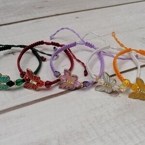May include: Five colorful bracelets with butterfly charms. Each bracelet is made with a different color of string and features a different colored butterfly charm.