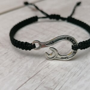 May include: Black braided bracelet with a silver wrench charm. The wrench has the word "Nine" engraved on it.