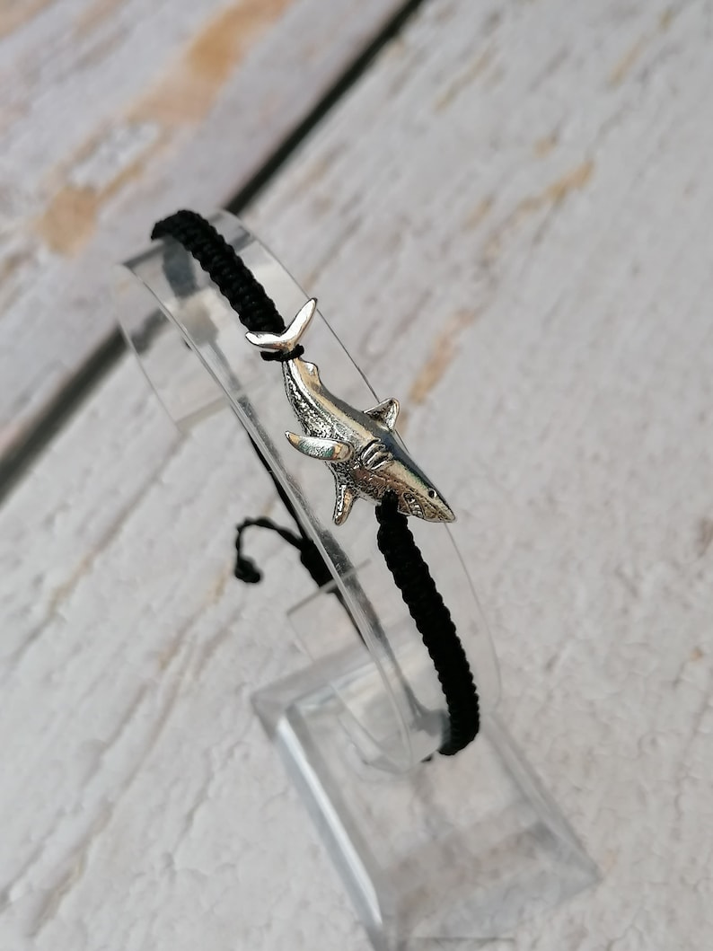May include: Black braided bracelet with a silver shark charm.