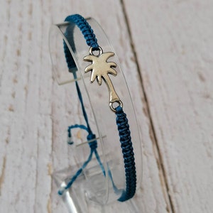 Puede incluir: Una pulsera trenzada azul oscuro con un dije de palmera de plata.