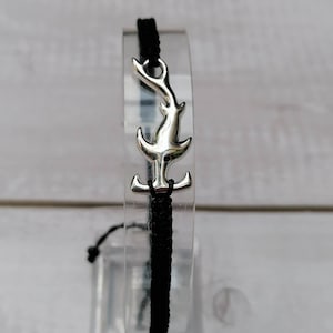 K&ouml;nnte beinhalten: Schwarzes geflochtenes Armband mit einem silbernen Hammerhai-Anh&auml;nger.
