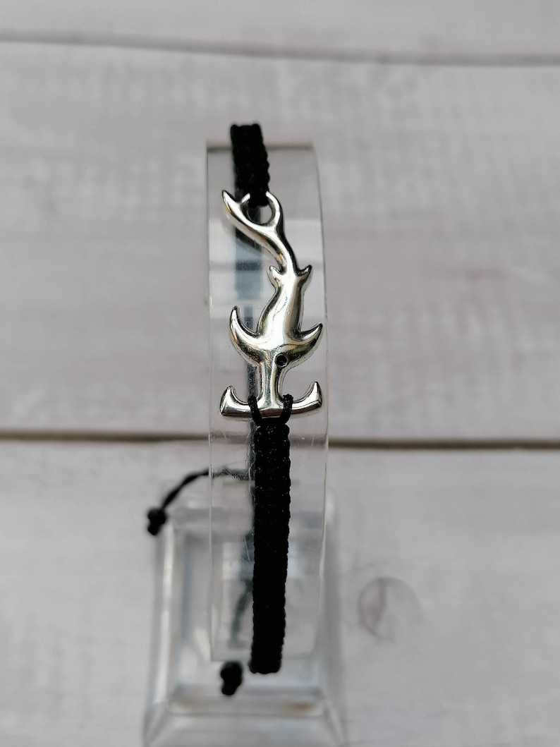 K&ouml;nnte beinhalten: Schwarzes geflochtenes Armband mit einem silbernen Hammerhai-Anh&auml;nger.