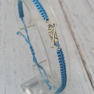 May include: A blue braided bracelet with a silver charm of a paddle and a surfboard.