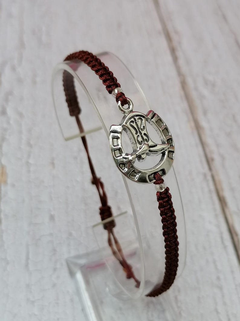 May include: A brown braided cord bracelet with a silver horseshoe charm featuring a boot design.