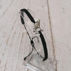 Puede incluir: Pulsera trenzada negra con un dije de lobo plateado.