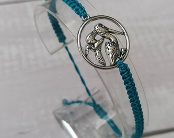May include: Teal braided bracelet with a silver charm featuring two pelicans in a circle.