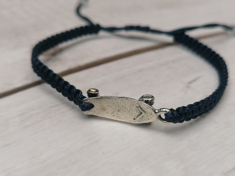 Puede incluir: Un brazalete de cord&oacute;n trenzado azul oscuro con un dije de patineta de plata.