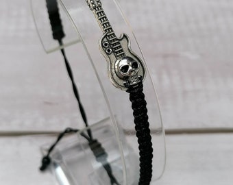 Peut inclure: Un bracelet en cordon tressé noir avec une breloque en métal argenté en forme de guitare électrique, intégrant un crâne sur le corps de l'instrument. Le bracelet présente une texture tissée et un mécanisme de fermeture réglable.