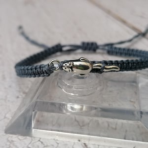 May include: A grey braided bracelet with a silver charm of an otter. The charm is attached to the bracelet with a silver ring.