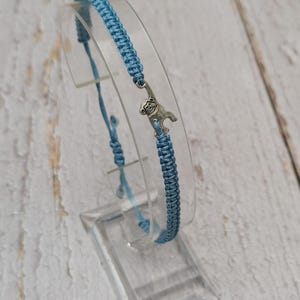 May include: A light blue braided bracelet with a silver charm of a monkey hanging from it.