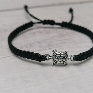 Puede incluir: Un brazalete trenzado negro con un dije de tortuga plateado. El brazalete es ajustable y se puede usar en la muñeca o el tobillo.