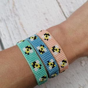 May include: Three beaded bracelets with a bee pattern. The bracelets are in shades of light blue, turquoise, and peach.