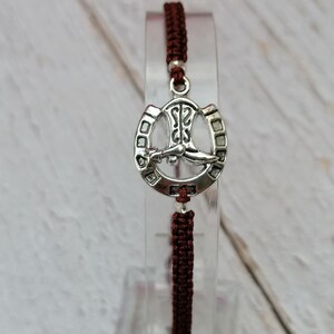 May include: A brown braided cord bracelet with a silver horseshoe charm featuring a boot inside.