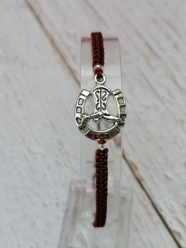May include: A brown braided cord bracelet with a silver horseshoe charm featuring a boot inside.