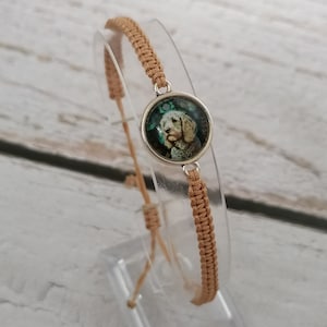May include: A tan braided bracelet with a round silver charm featuring a white dog with black spots. The charm has a green and blue background.