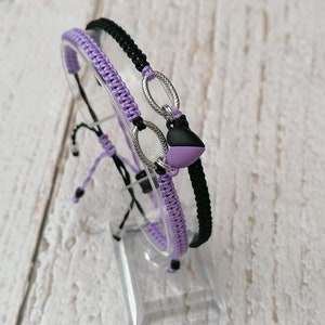May include: Two friendship bracelets, one purple and one black, with a silver charm and a purple and black heart charm.