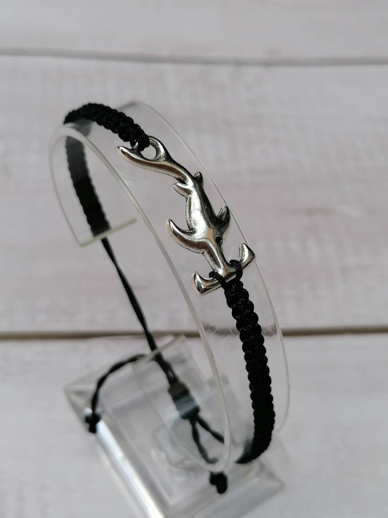 K&ouml;nnte beinhalten: Ein Armband aus schwarzem Band mit einem silbernen Hammerhai-Anh&auml;nger.
