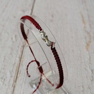 May include: A red string bracelet with a silver mermaid charm. The bracelet is tied with a knot and has a sliding knot for adjusting the size.