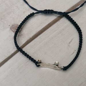 Puede incluir: Un brazalete de cord&oacute;n trenzado negro con un dije de patineta de plata.