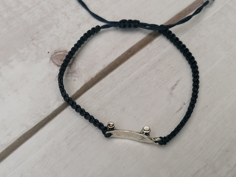 Puede incluir: Un brazalete de cord&oacute;n trenzado negro con un dije de patineta de plata.