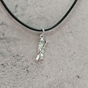 Pode incluir: Colar com pingente prateado com design de prancha de surf e remo. O pingente pende de um cordão preto. A prancha de surf tem um design em espiral e é uma pequena e detalhada peça de joalharia.