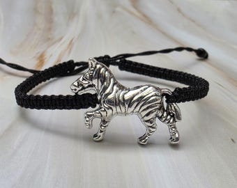 Op de afbeelding: Een zwart macramé armband met een zilverkleurige zebra bedel. De zebra bedel is gedetailleerd met strepen en is het middelpunt van de armband. De armband is verstelbaar en geschikt voor verschillende polsmaten.