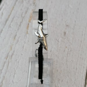 May include: A black cord bracelet with a silver shark charm.
