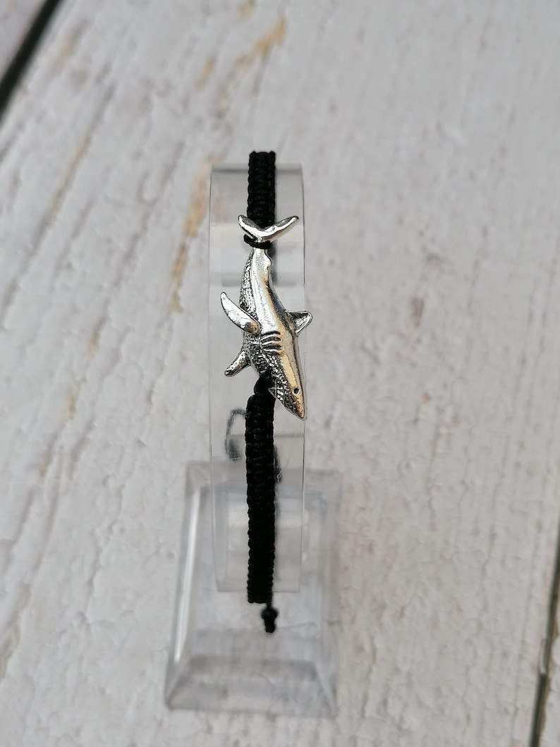 May include: A black cord bracelet with a silver shark charm.