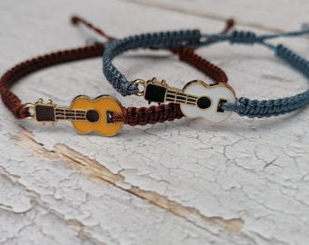 May include: Two friendship bracelets with guitar charms. One bracelet is brown and the other is blue. The guitar charms are yellow and white.