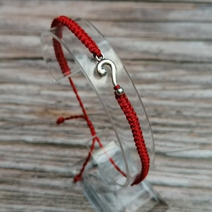 Puede incluir: Pulsera de cuerda roja con un dije de plata en forma de signo de interrogación.