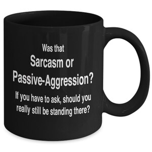 May include: Black ceramic coffee mug with white text that reads "Was that Sarcasm or Passive-Aggression? If you have to ask, should you really still be standing there?"
