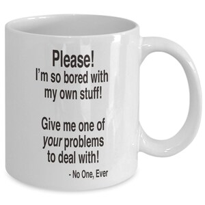 Könnte beinhalten: Weiße Keramik-Kaffeetasse mit schwarzem Text, der lautet: "Bitte! Ich langweile mich so mit meinen eigenen Sachen! Gib mir eines deiner Probleme, mit denen ich mich befassen kann! - Niemand, jemals"