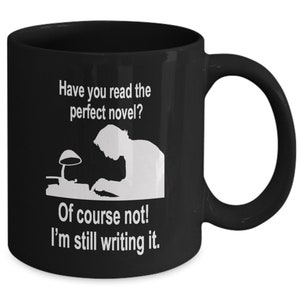 May include: Black coffee mug with white text that reads "Have you read the perfect novel? Of course not! I'm still writing it."  The mug also features a silhouette of a person writing at a desk with a lamp.