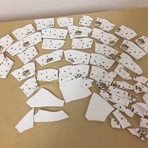 May include: A collection of white ceramic tiles with a colorful confetti pattern. The tiles are broken into various shapes and sizes.