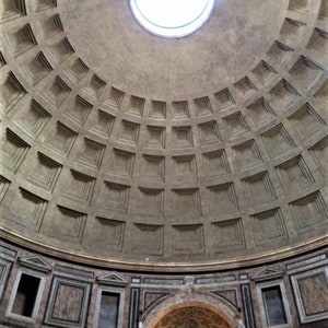 May include: An upward view of the interior of a domed ceiling with a circular opening at the top. The ceiling is gray with a grid-like pattern of recessed squares. The lower portion features decorative panels and arched details.