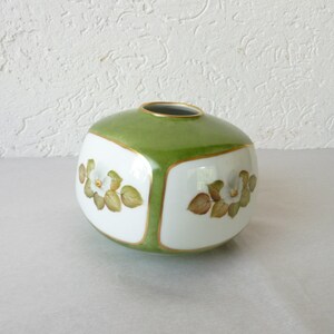 May include: A green and white ceramic vase with a square shape and floral designs. The vase has a gold trim around the edges.