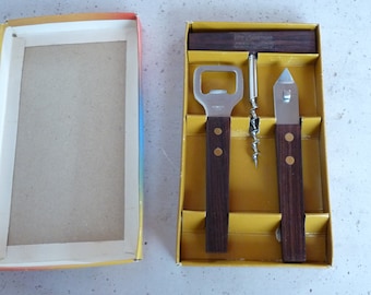 Op de afbeelding: Een set van drie keukenhulpmiddelen met houten handvatten in een gele doos. De hulpmiddelen omvatten een flessenopener, een kurkentrekker en een blikopener.