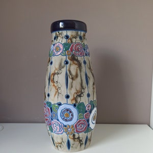 Op de afbeelding: Een keramische vaas met een marmerpatroon in tinten bruin, wit en blauw. De vaas is versierd met een band van kleurrijke bloemen en bladeren.