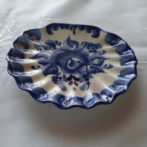 May include: A white ceramic plate with a blue floral design. The plate has a scalloped edge and is decorated with a blue and white floral pattern.